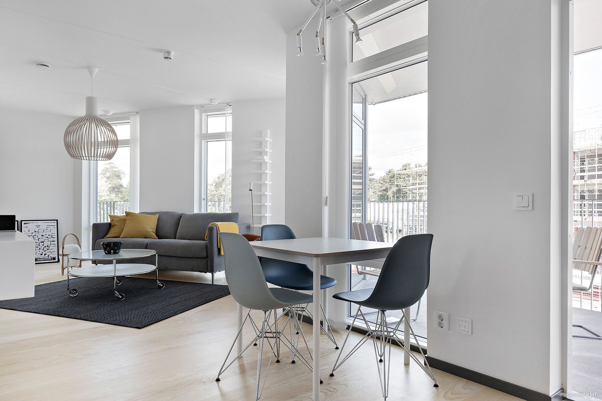 A modern living room with a grey sofa, a dining table with chairs, and large windows offering a view of the city.