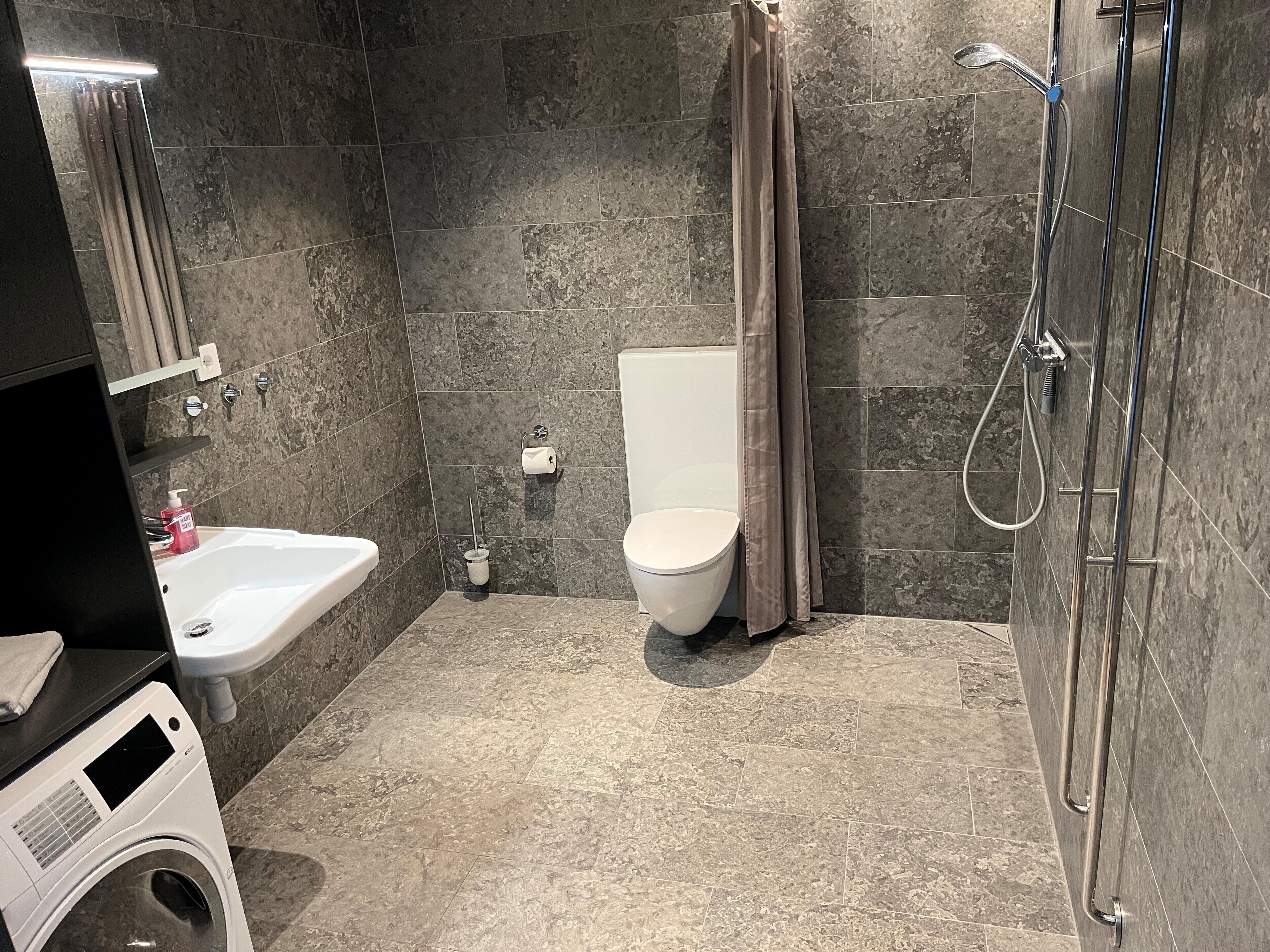A modern bathroom with a white sink, toilet, and shower area.