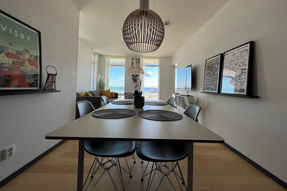 Een moderne eetruimte met een grote tafel, zwarte stoelen en een bijzondere hanglamp.