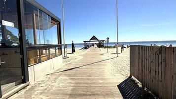 A beach walkway with a wooden fence, a covered seating area, and a building with large windows.
