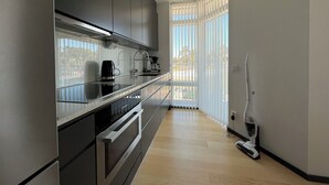 Moderni keittiö, jossa on ruostumattomasta teräksestä valmistetut kodinkoneet, lasinen työtaso ja suuret ikkunat, joista on näkymä ulos.