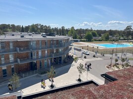 A multi-story building with a brick facade and balconies, a parking area with a swimming pool, and a clear sky.