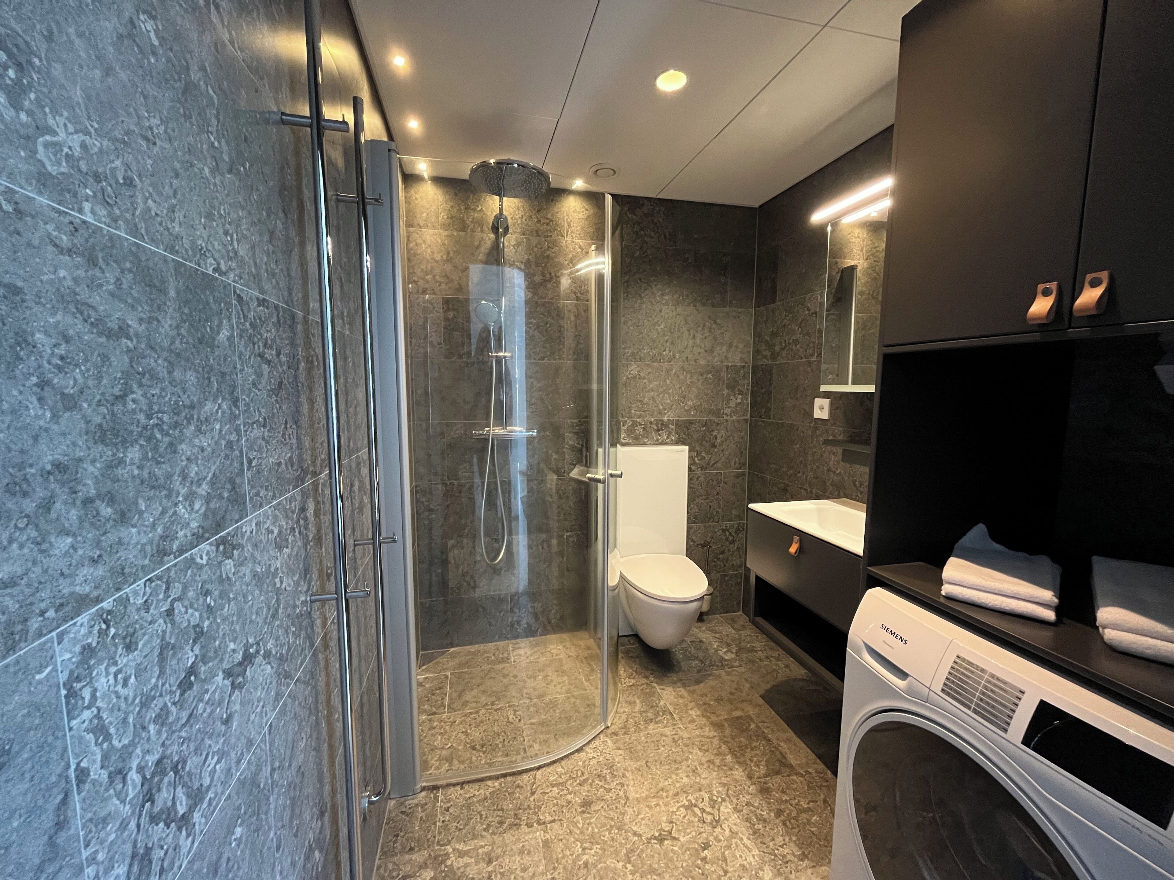 Un baño moderno con ducha de vidrio, inodoro, lavabo y lavadora.