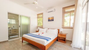 Un dormitorio con cama, mesitas de noche, ventilador de techo, equipo de aire acondicionado y una ventana con persianas.