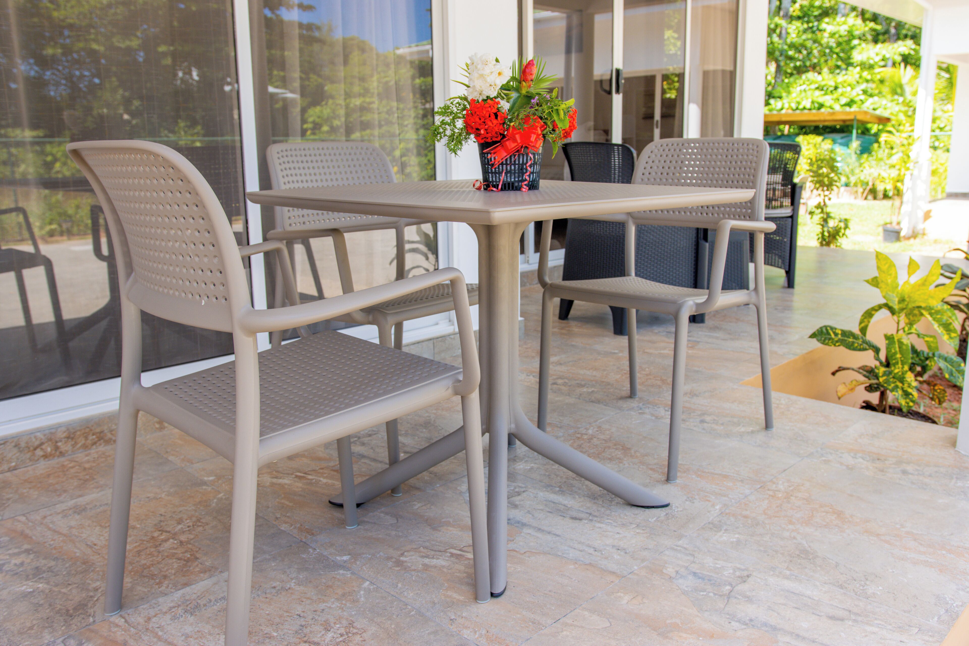 An outdoor patio with a table and chairs, a vase with flowers, and a view of the garden.