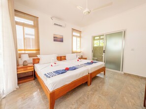 A double bed with a wooden frame, two bedside tables with lamps, a ceiling fan, and a sliding glass door leading to a bathroom.