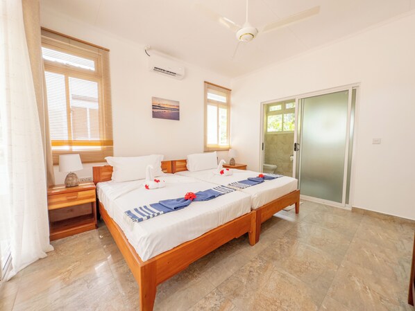A double bed with a wooden frame, two bedside tables with lamps, a ceiling fan, and a sliding glass door leading to a bathroom.