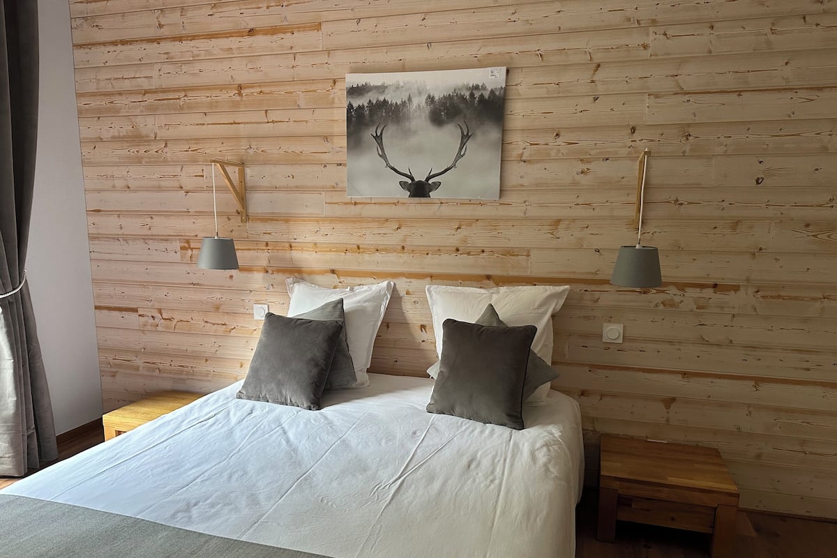 A bedroom with a wooden headboard, a bed with white bedding and gray pillows, two bedside tables, and a wall-mounted painting of a deer.
