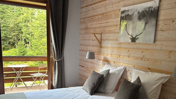 Un dormitorio con una cama grande, cabecera de madera, un cuadro de un ciervo y vistas a un bosque desde la ventana.