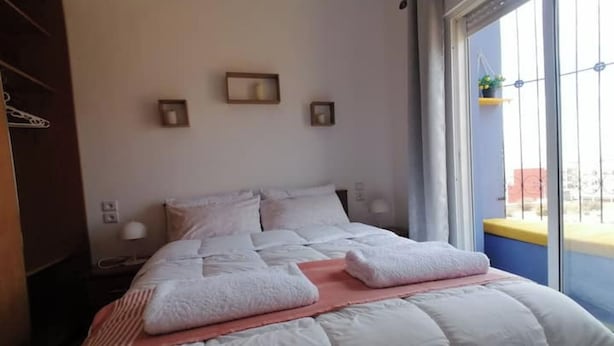 Ein ordentlich gemachtes Bett mit weißer Bettwäsche und zwei gefalteten Handtüchern, ein Nachttisch mit Lampe und ein Fenster mit Blick ins Freie.