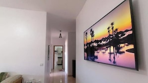 Ein Flur mit einem großen Gemälde, das einen Sonnenuntergang über Wasser zeigt, einer Tür, die in einen anderen Raum führt, und einem kleinen Tisch mit Gegenständen darauf.