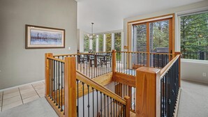 Un espacio interior amplio con una escalera de madera, ventanas grandes y vistas al exterior.
