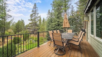 A wooden deck with a table and chairs, surrounded by a black metal railing, overlooking a forested area.
