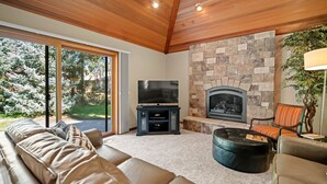A modern living room with a stone fireplace, a large flat-screen TV, and comfortable seating. - Sunriver Retreat with Access to The Cove (Sunriver)
