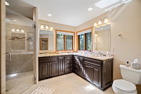 A modern bathroom with a glass shower enclosure, dark cabinetry, and a large vanity with a sink and mirror.