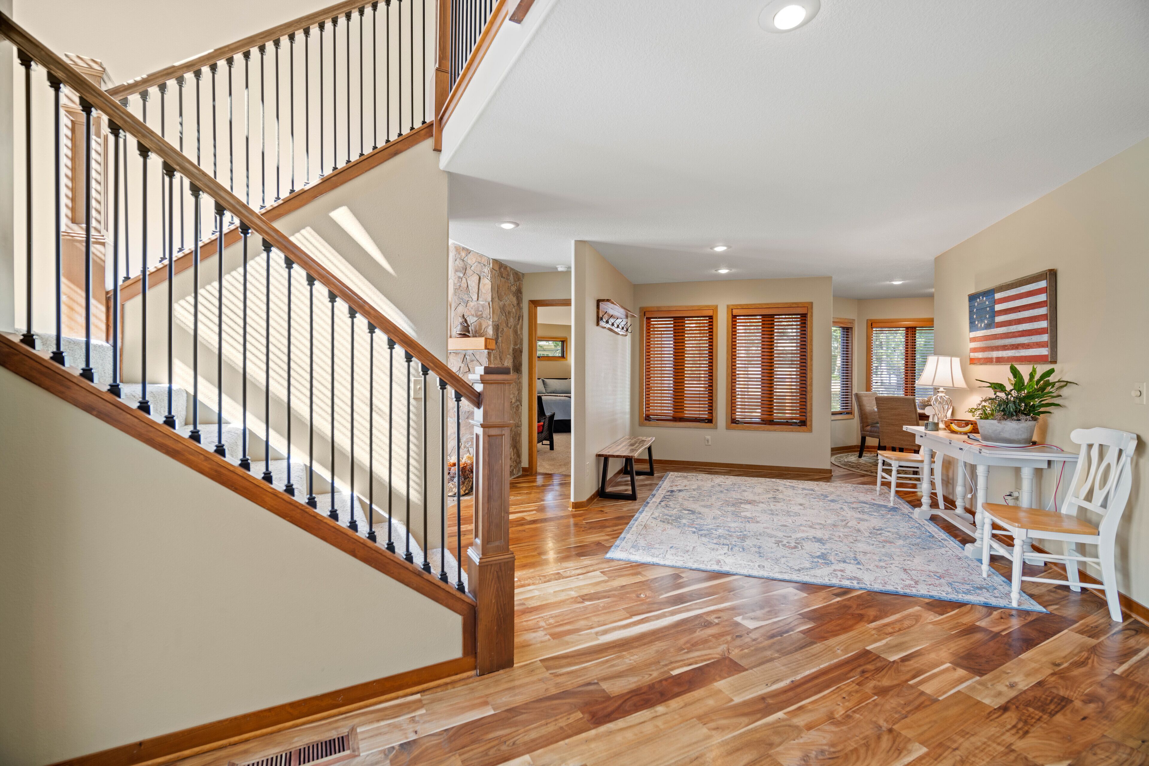 A spacious living area with a wooden staircase, a large rug, and a dining table with chairs.