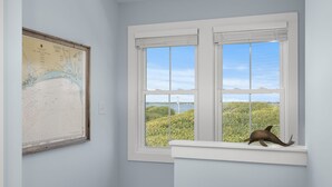 A room with a large map on the wall, a window with a view of greenery and water, and a dolphin figurine on the windowsill. - Judi's Place, Oceanfront House in Salter Path, NC! (Salter Path)