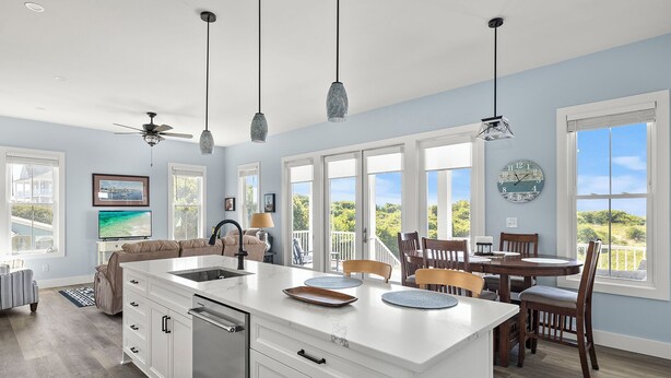 A modern kitchen with a central island, large windows, and a dining area with wooden chairs. - Judi's Place, Oceanfront House in Salter Path, NC! (Salter Path)