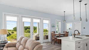 A modern kitchen with a white island, wooden chairs, and a dining table. - Judi's Place, Oceanfront House in Salter Path, NC! (Salter Path)