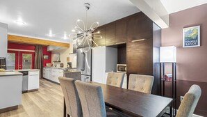 Eine moderne Küche mit Edelstahlgeräten, ein Essbereich mit Holztisch und gepolsterten Stühlen sowie eine Wand in Rot als Akzent.