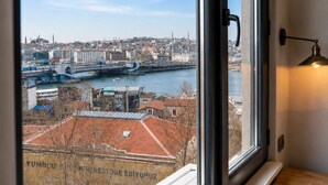 A room with a large window overlooking a cityscape, a door, and a wall-mounted lamp. - ART Karakoy Hotel (Istanbul)