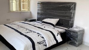 A bedroom with a bed, a nightstand, a window with bars, and a tiled floor. - Inviting 8 Bed House in Lekki (Lekki)