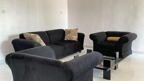 A modern living room with a black sofa set and a matching armchair, a coffee table, and a patterned throw pillow. - Inviting 8 Bed House in Lekki (Lekki)