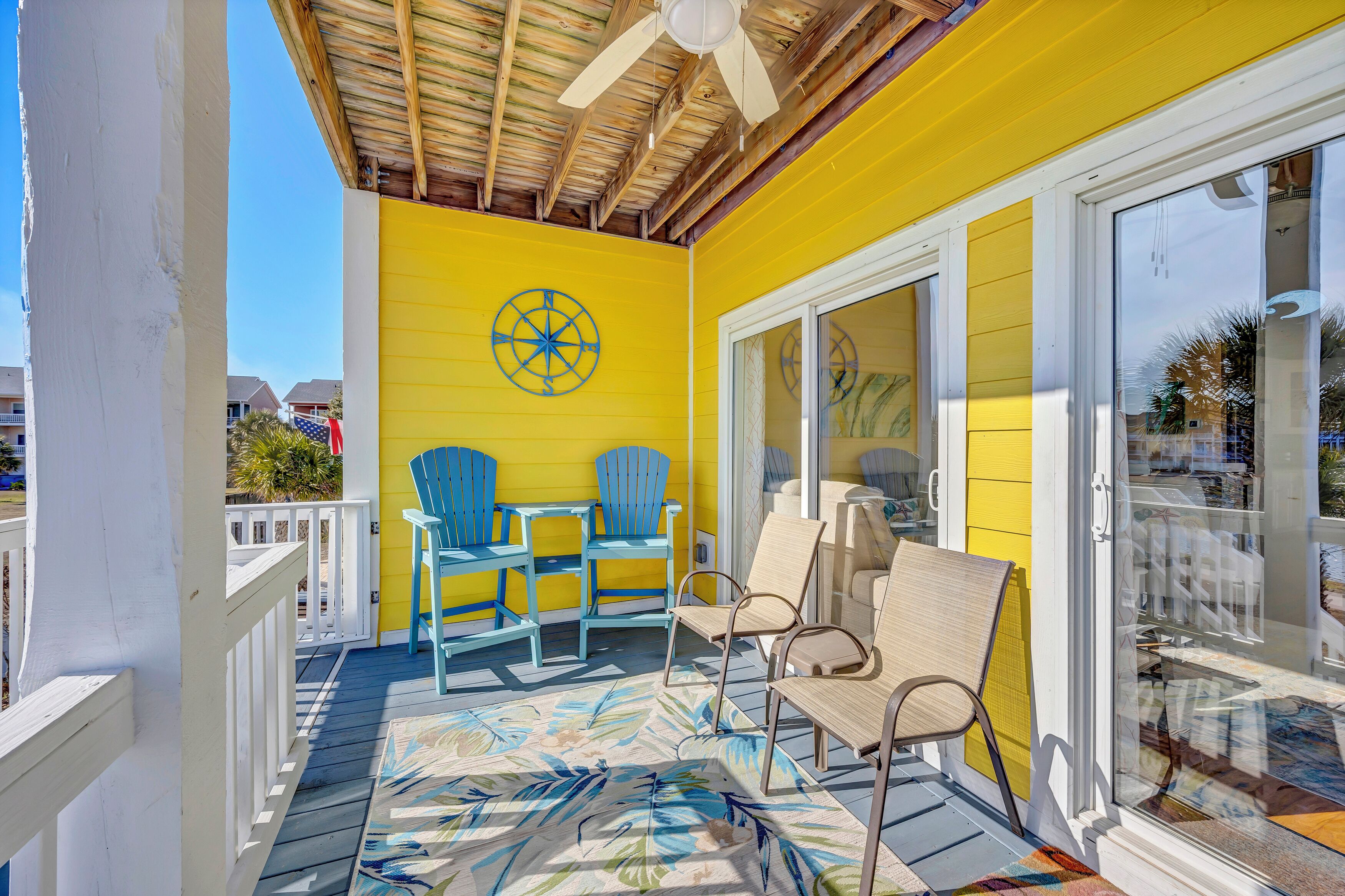 A bright yellow room with a ceiling fan, a large window, and a tropical-themed rug.