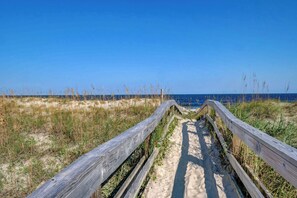 A wooden boardwalk leading to the beach, surrounded by sand and grass. - Stay, Play, Relax: Pet-Friendly Oasis in the heart of Carolina Beach (Carolina Beach)