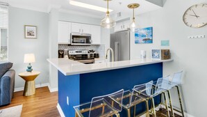 A modern kitchen with a blue accent wall, stainless steel appliances, and clear glass bar stools.