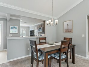 A dining area with a wooden table and chairs, a chandelier, and a kitchen in the background. - Stay in Style near the Golf Course in the Village of Fenney! (The Villages)