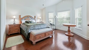 A bedroom with a wooden bed, two bedside tables, a floor lamp, a standing lamp, a ceiling fan, and a window with blinds. - 3/2 Designer with a Golf Cart, close to Lake Sumter & Brownwood!!! (The Villages)