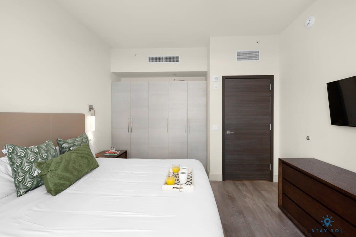 A hotel room with a bed, a bedside table, a wardrobe, a TV, and a dresser.