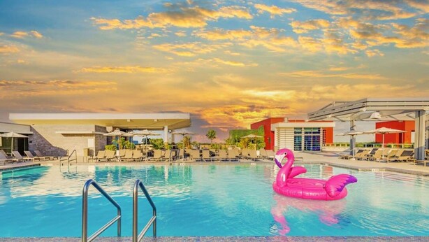 Une piscine avec un flotteur en forme de flamant rose, des chaises longues et un bâtiment moderne en arrière-plan.