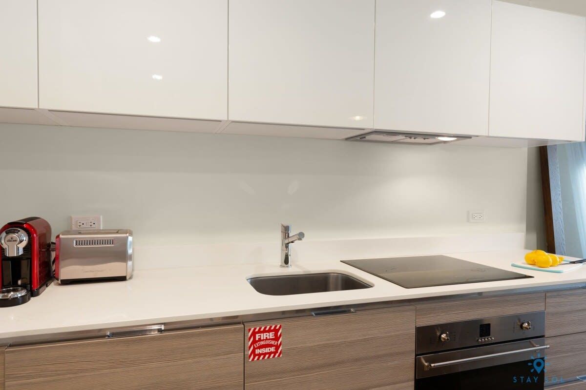 Una cocina moderna con armarios blancos, un lavamanos de acero inoxidable, un tostador y un letrero de extintor.