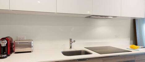 Una cocina moderna con armarios blancos, un lavamanos de acero inoxidable, un tostador y un letrero de extintor.