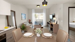 Un espace de repas moderne avec une table dressée pour quatre personnes, un canapé, un téléviseur et une vue sur l’extérieur.