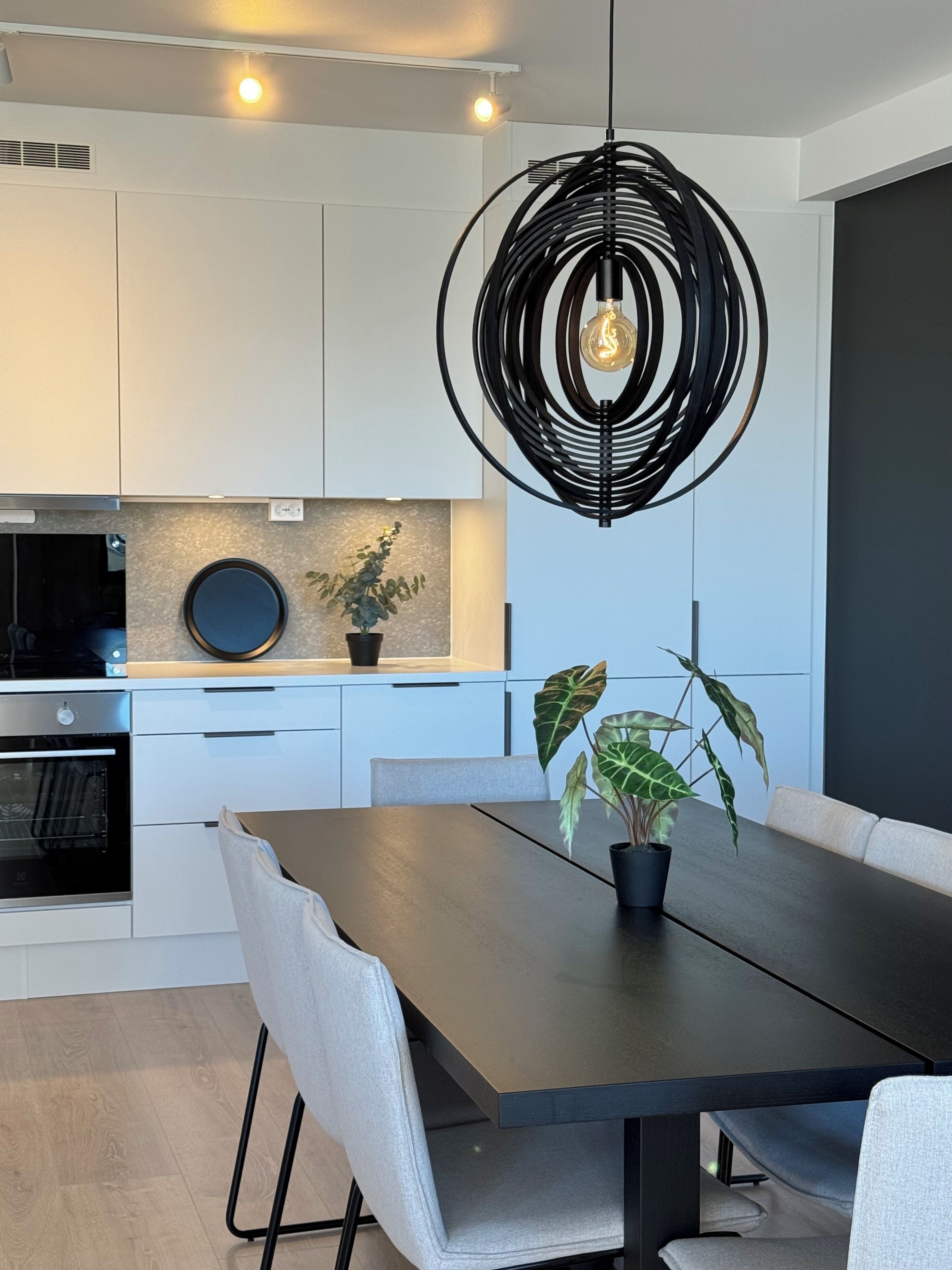 Una cucina moderna con mobili bianchi, forno integrato e zona pranzo con tavolo e sedie in legno scuro.