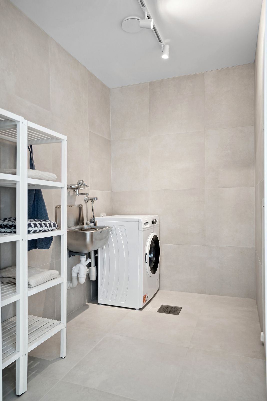 A modern laundry room with a built-in washing machine and a metal sink.