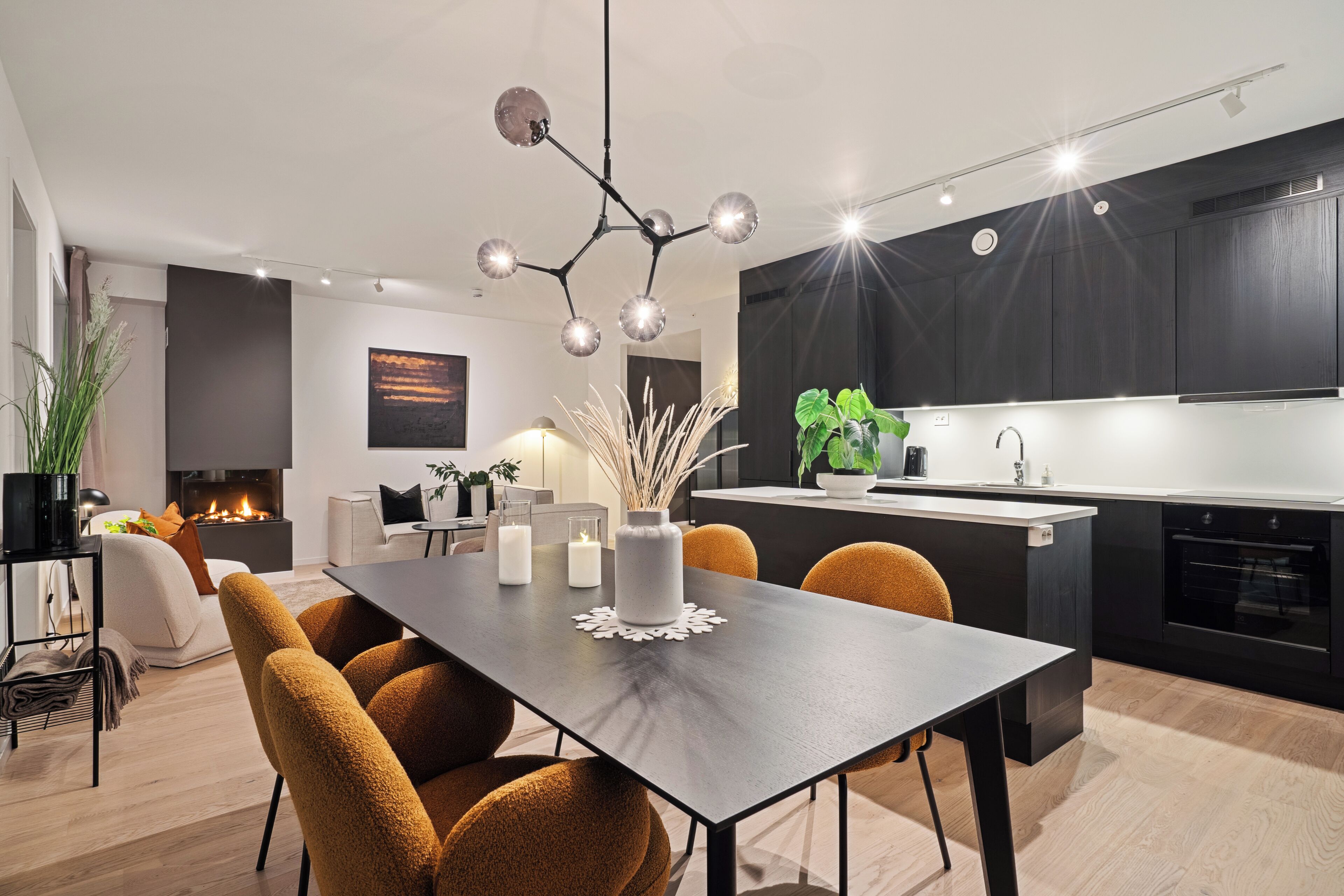 A modern kitchen with dark cabinets, a central island, and a dining area with a dark table and mustard-colored chairs.