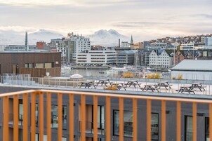 Un paisaje urbano con edificios modernos, una marina con barcos y montañas nevadas al fondo.