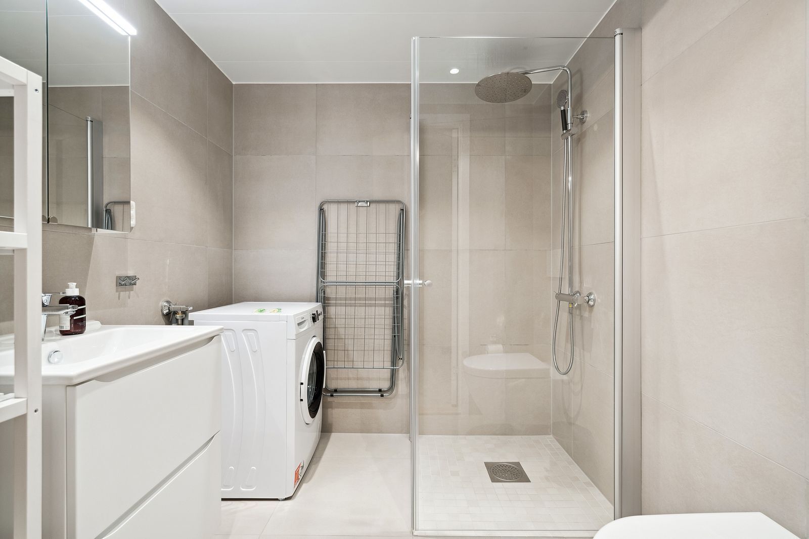 A modern bathroom with a glass-enclosed shower, a washing machine, and a toilet.