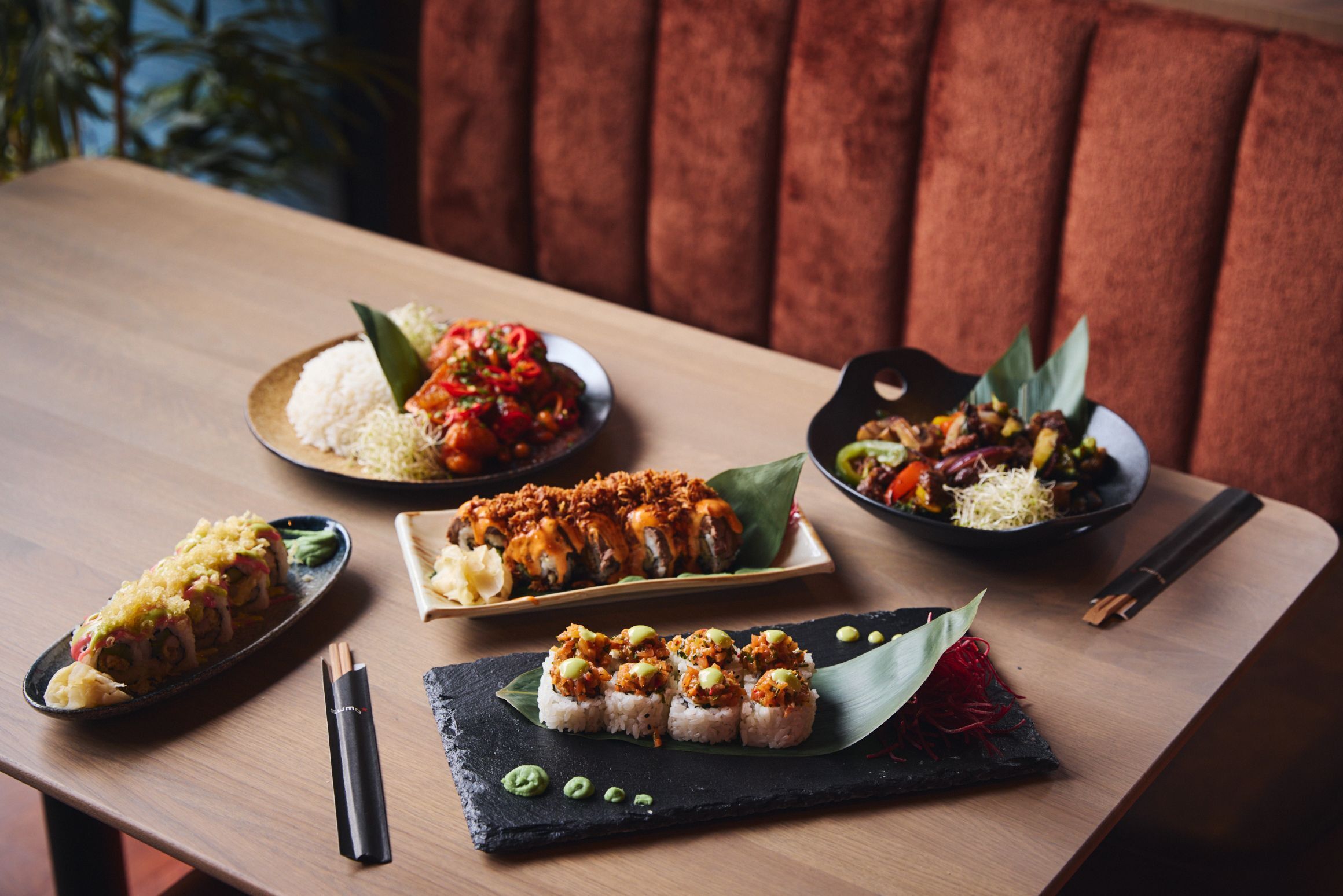 Ein Tisch mit verschiedenen Gerichten, darunter Sushi, Reis und Gemüse, mit Stäbchen und einer schwarzen Serviette.