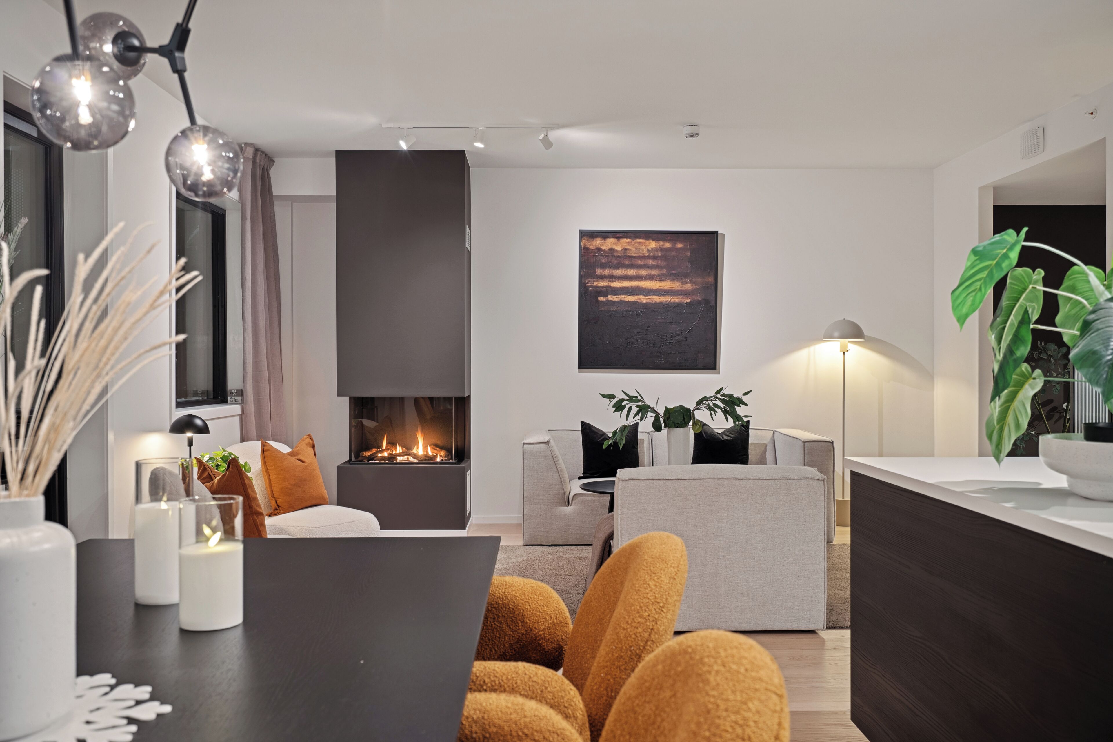 A modern living room with a fireplace, a dining area with candles, and a large plant.