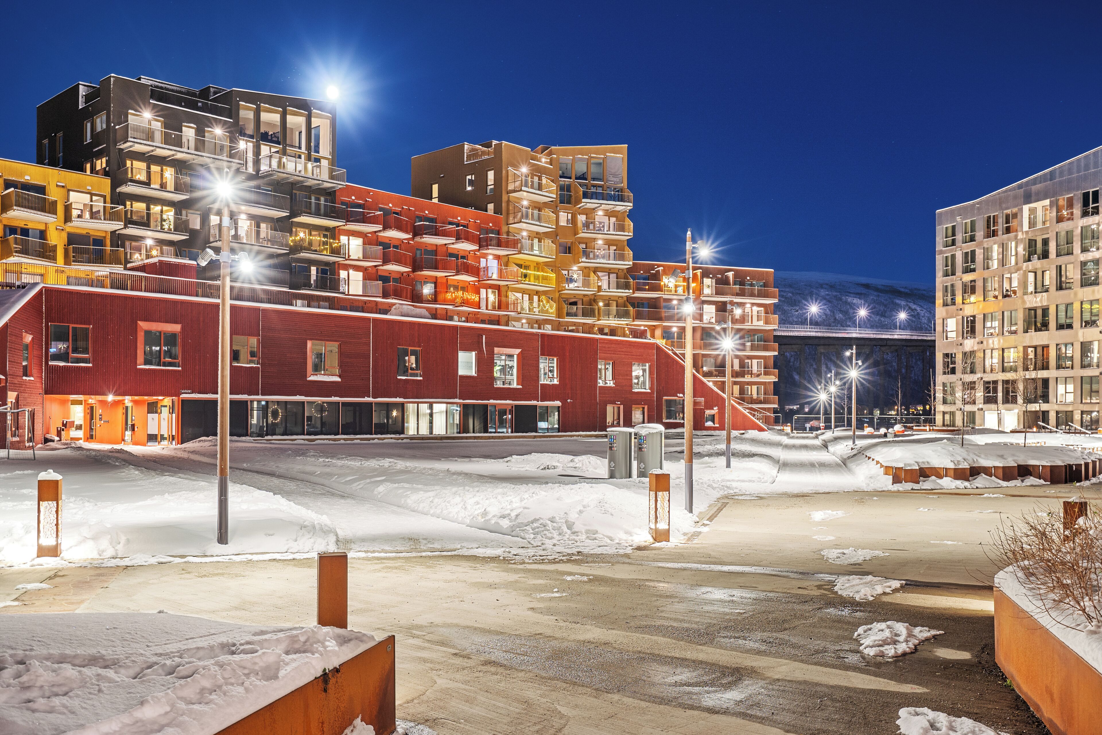 Un hotel de varios pisos con balcones, suelo cubierto de nieve y farolas.