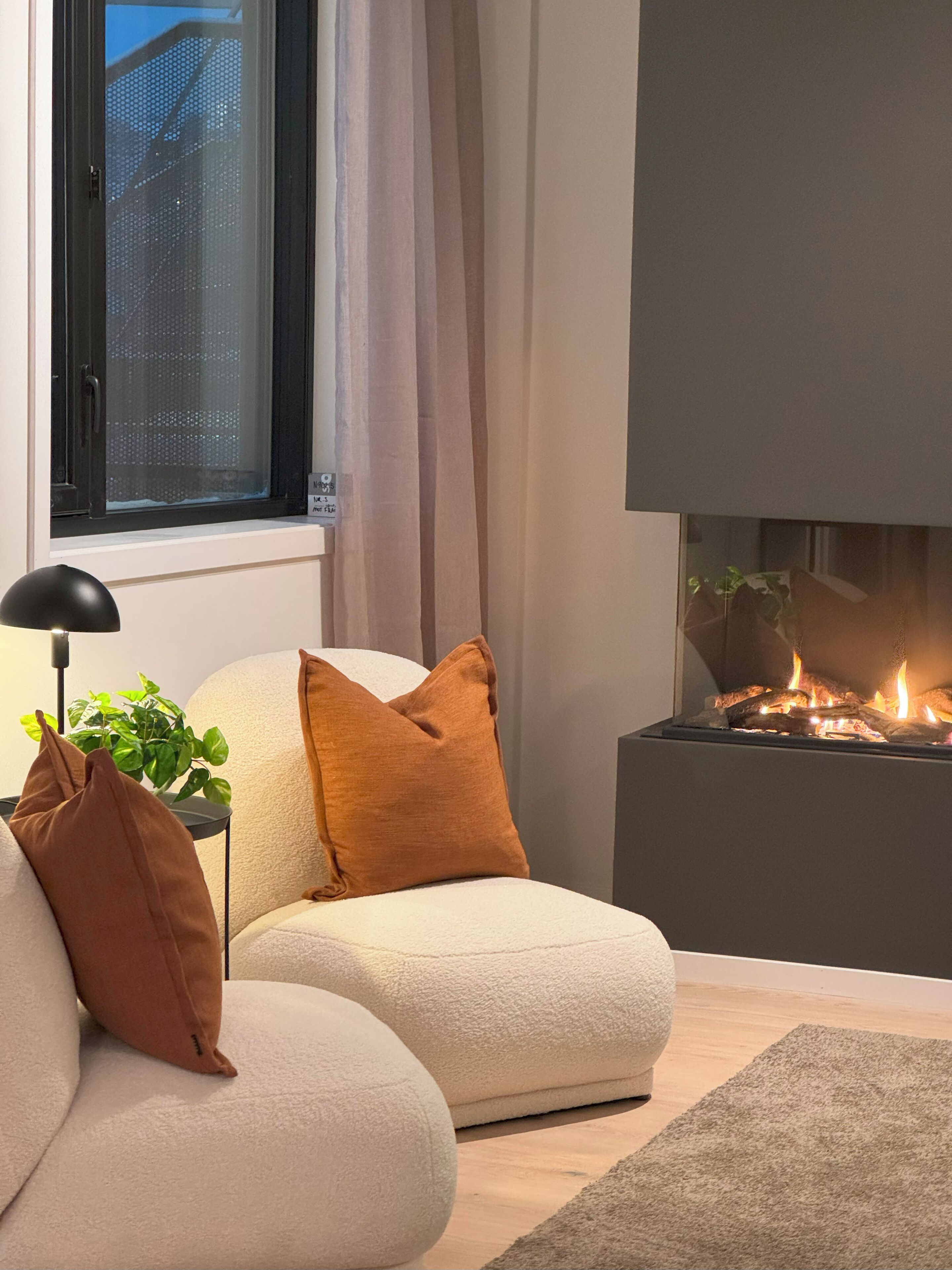 Una sala de estar moderna con un sofá, cojines, una lámpara de pie, una chimenea y un ventanal con cortinas.
