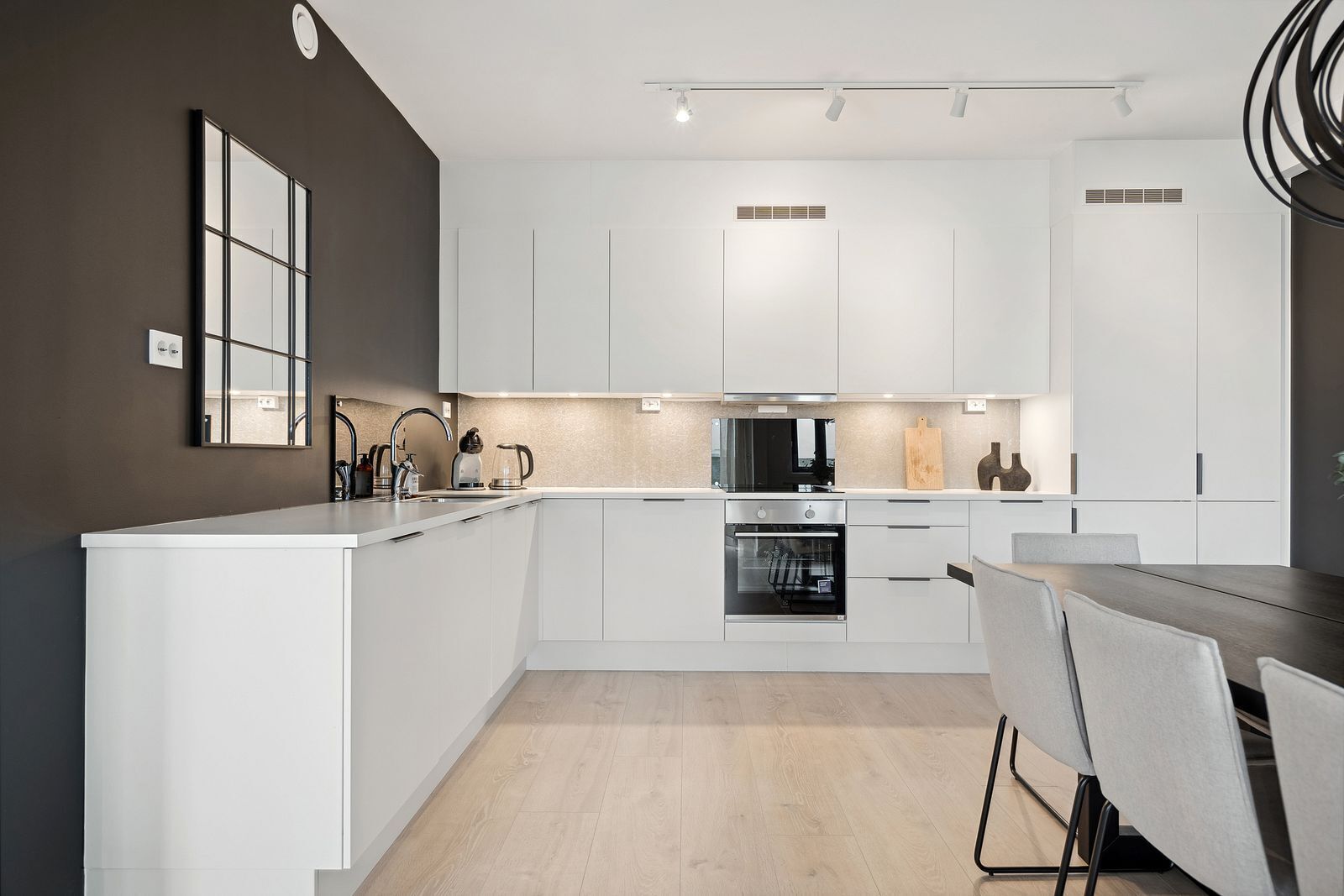 Une cuisine moderne avec des meubles blancs, un îlot central et un coin repas comprenant une table et des chaises.