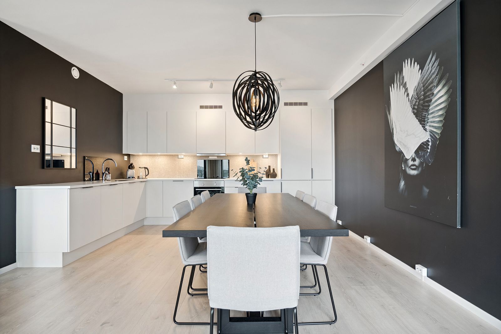 A modern kitchen with white cabinets, a central island, and a dining area with a long table and chairs.
