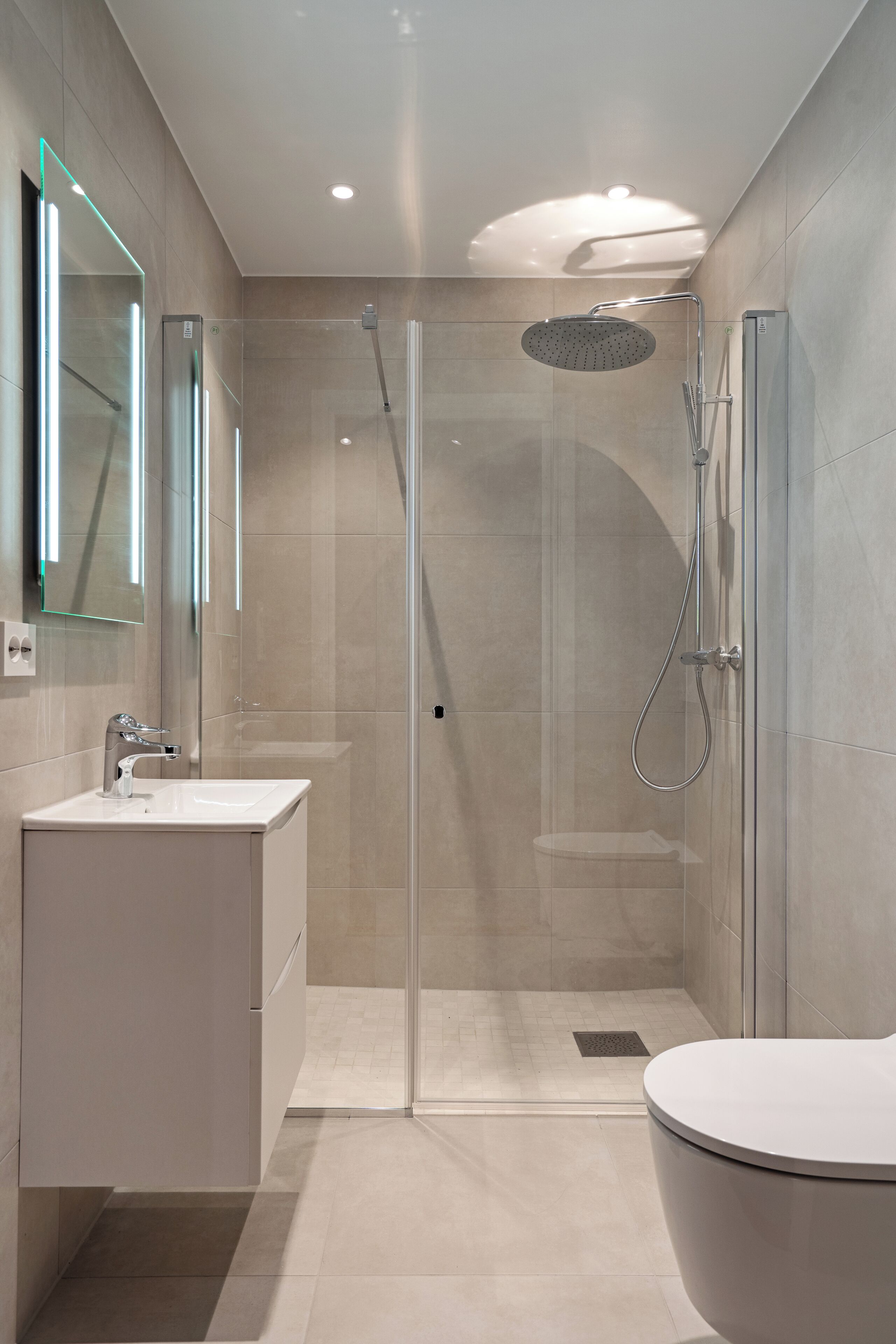 Un baño moderno con cabina de ducha de vidrio, un lavabo blanco y un inodoro.