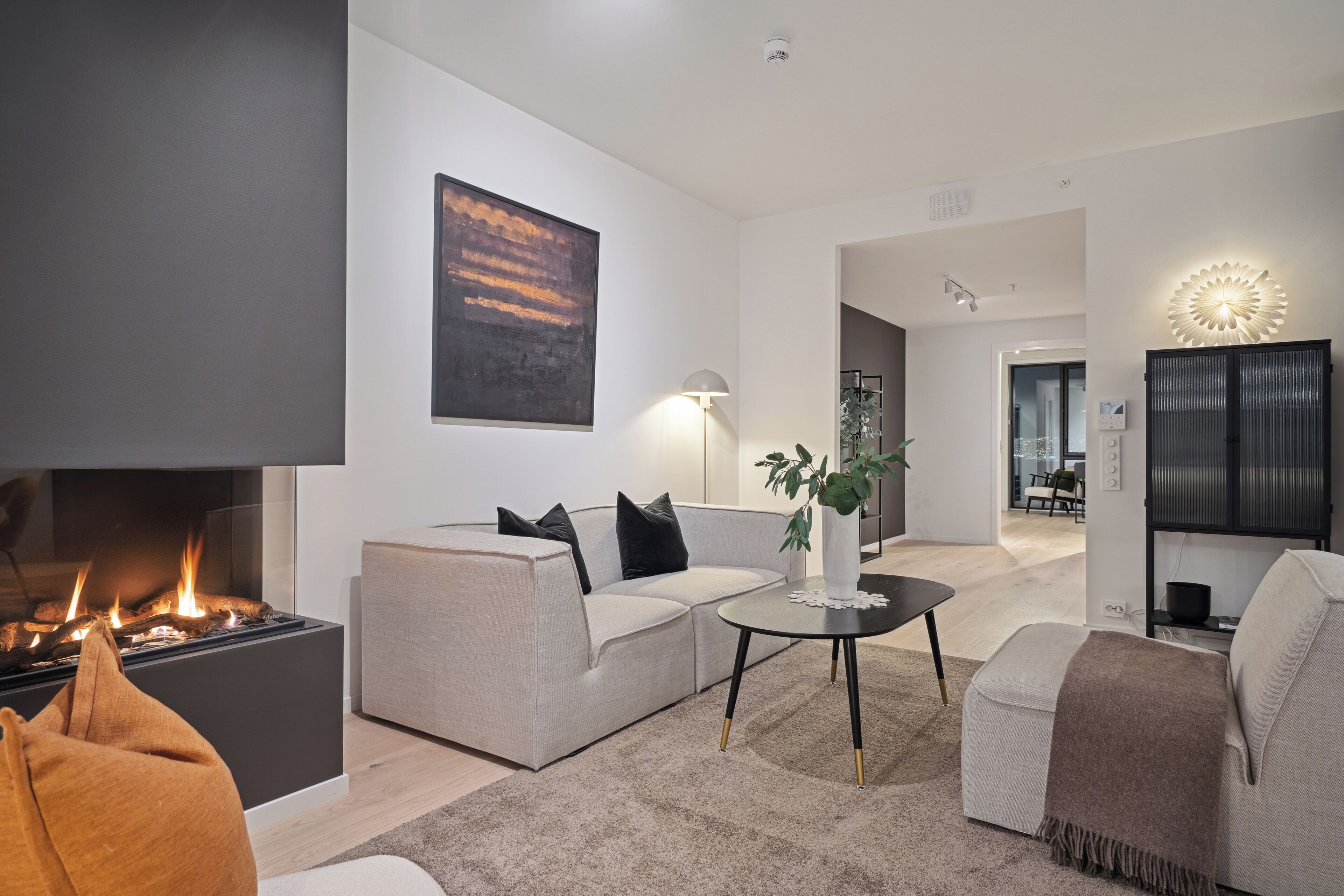 A modern living room with a fireplace, sofas, a coffee table, and a decorative wall piece.